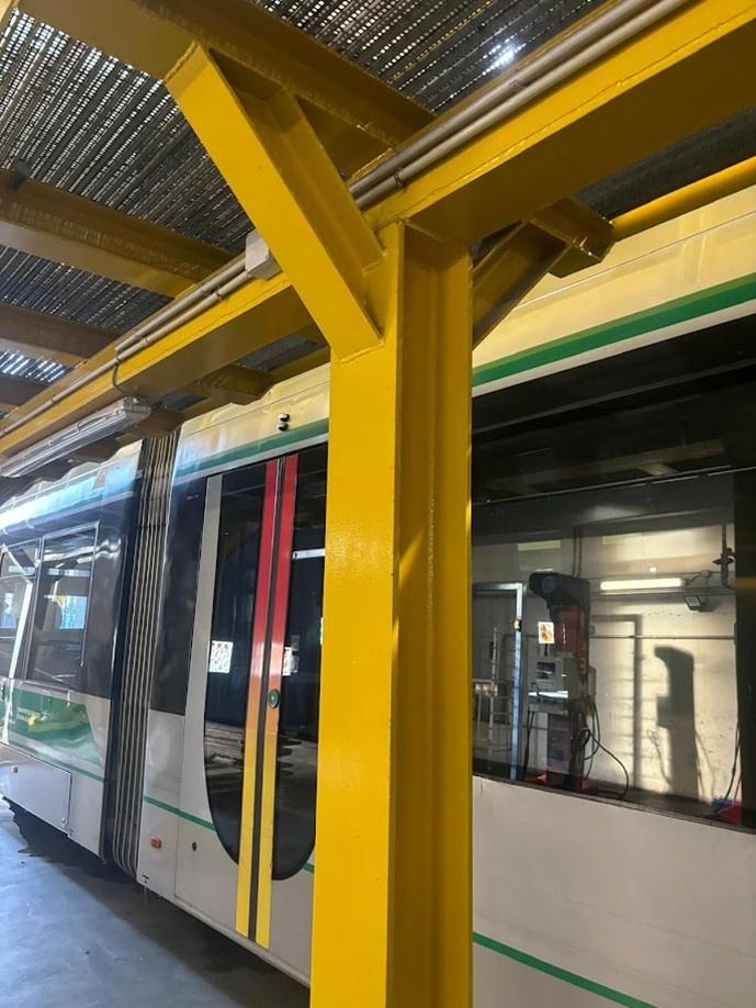 Estructura metálica amarilla instalada junto a un tren del metro de Sevilla, correspondiente a la pasarela de mantenimiento diseñada y calculada en el proyecto.
